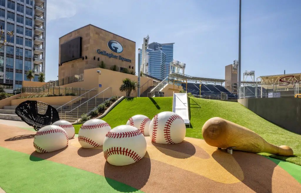 Gallagher Square at Petco Park by Landrec — oversized baseball sculptures and a metal embankment slide on a turf berm, one of the projects behind our custom slide pricing