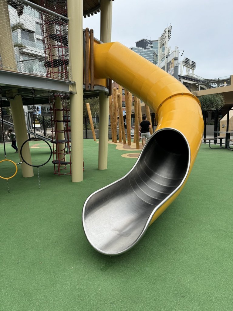 Custom yellow tube slide with stainless steel exit at Gallagher Square, built by Landrec